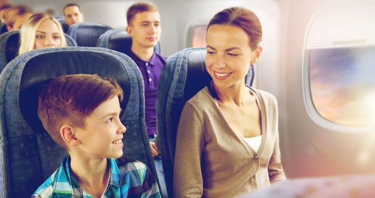 a imagem apresenta uma mãe e seu filho sentados dentro de um avião, eles estão lado a lado sorrindo um para o outro.