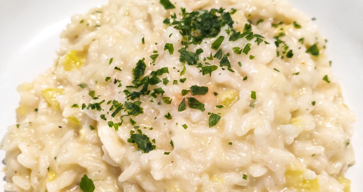 imagem de um prato branco com um risoto de alho-poró servido com salsinha decorando o prato.