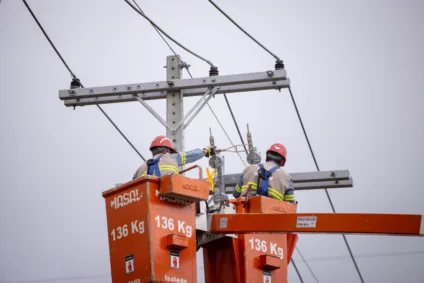 Dois trabalhadores em um caminhão de elevação realizando reparos em linhas de energia elétrica. Eles estão usando equipamentos de segurança e capacetes.