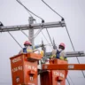 Dois trabalhadores em um caminhão de elevação realizando reparos em linhas de energia elétrica. Eles estão usando equipamentos de segurança e capacetes.