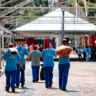 Grupo de trabalhadores em camisetas azuis caminhando pelo Centro Histórico de Porto Alegre, carregando equipamentos e utensílios de varrição.