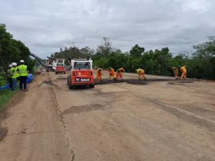 Trabalhadores em obras no quilômetro 46 da FreeWay, com máquinas e equipamentos de construção em um dia nublado.