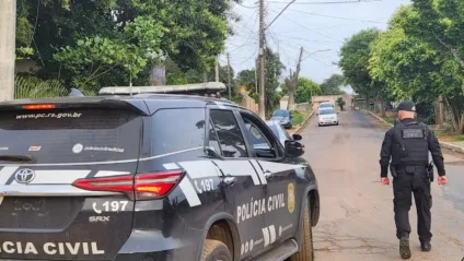 Veículo da Polícia Civil estacionado em uma rua, com um policial em uniforme tático, observando o ambiente ao redor.