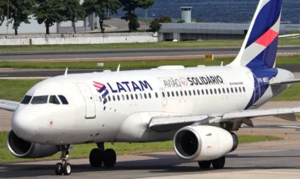 Avião Airbus A319 da LATAM com a inscrição "Avião Solidário" em uma pista, rodeado por vegetação e infraestrutura aeroportuária.