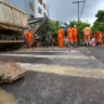 Trabalhadores em uniforme laranja realizando reparo de adutora na avenida Coronel Lucas de Oliveira, em Porto Alegre, com caminhão e máquinas.