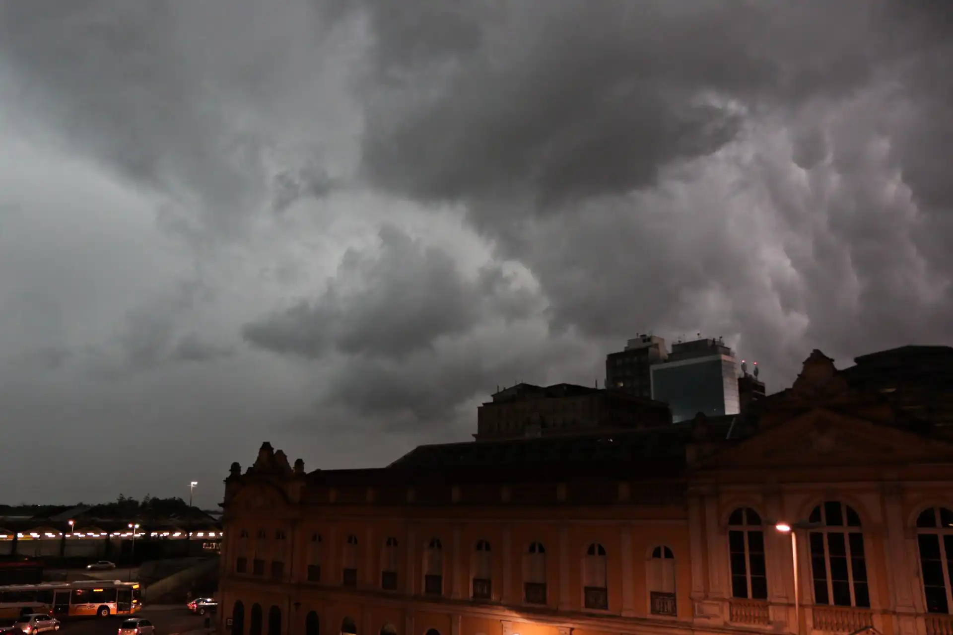 Céu nublado com nuvens escuras sobre edifícios e luzes do Centro de Porto Alegre durante a noite.