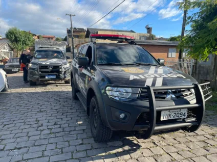 Carros da Polícia Civil do RS estacionados em uma rua de paralelepípedos, com agentes da polícia próximos.