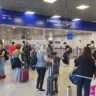 Passageiros aguardando embarque doméstico no Aeroporto Salgado Filho. Eles transportam malas e mochilas e o ambiente está movimentado.