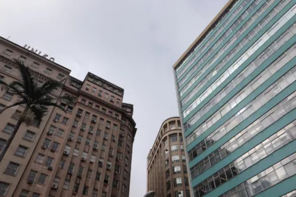 Vista do Centro de Porto Alegre em um dia nublado, com edifícios históricos e modernos, incluindo detalhes de janelas e uma palmeira.