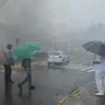 Cena de desastre em Gramado após queda de avião. Pessoas se protegem da chuva enquanto observam os danos e fumaça no local.