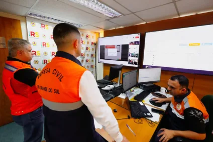 Equipe da Defesa Civil do Rio Grande do Sul atuando em sala de monitoramento. Monitores exibem informações durante teste do sistema Defesa Civil Alerta