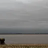 Vista do Cais do Porto em Porto Alegre, destacando o imponente céu cinza e o cais de pedra ao lado da água serena.