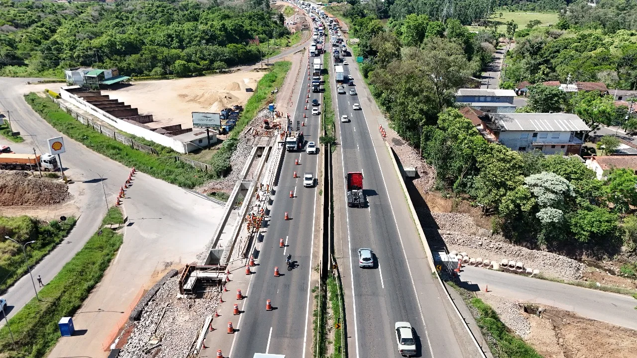 Vista aérea das obras na BR-386, em Estrela, com várias faixas de tráfego e cones de sinalização, rodeada por vegetação.