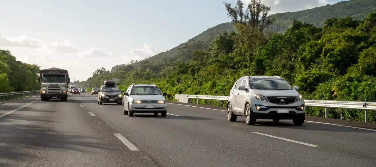 Imagem da FreeWay com diversos veículos, incluindo caminhões e carros, rodeada por vegetação e montanhas, representando o tráfego em rodovias.