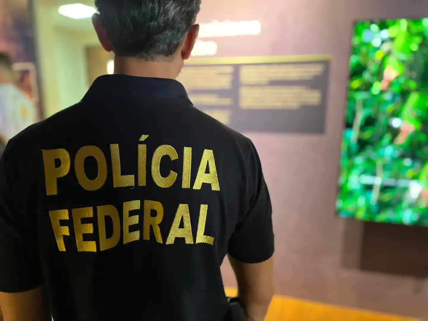 Membro da Polícia Federal em um ambiente institucional, mostrando a camisa com a inscrição 'Polícia Federal' em destaque.