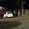 Imagem noturna de um veículo branco com a porta aberta, cercado por policiais.