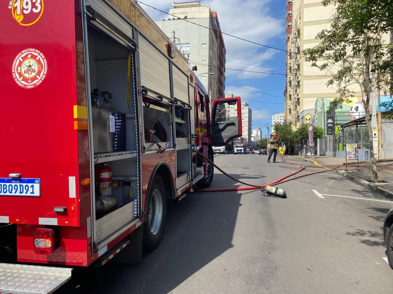 Imagem de um caminhão de bombeiros estacionado na rua durante uma ação de combate a incêndio, com mangueiras e equipes em atividade.