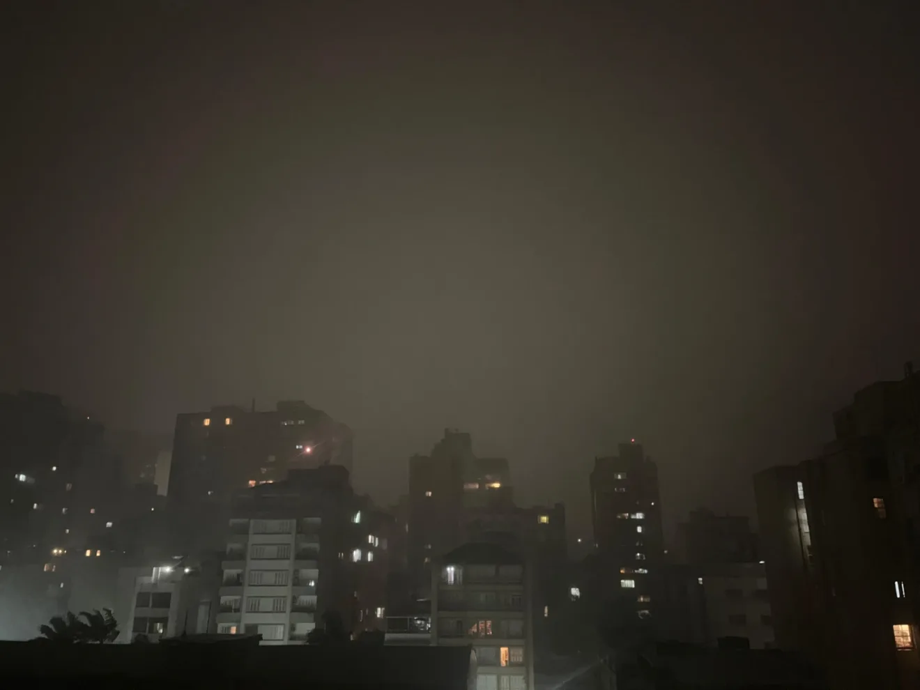 Vista da cidade de Porto Alegre durante um temporal, com chuvas intensas e prédios visíveis sob um céu escuro e nebuloso.