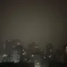 Vista da cidade de Porto Alegre durante um temporal, com chuvas intensas e prédios visíveis sob um céu escuro e nebuloso.