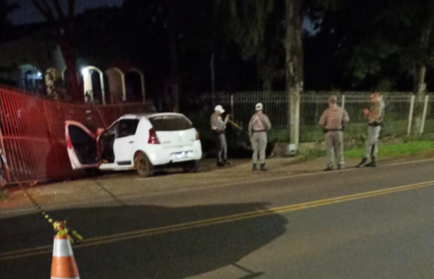 Imagem noturna de um veículo branco com a porta aberta, cercado por policiais.