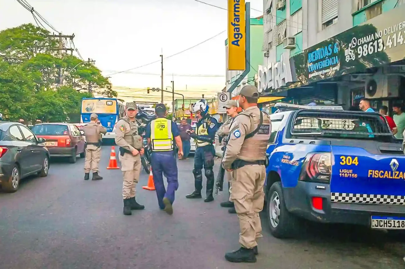 Imagem de policiais em operação em uma rua da cidade, com viaturas e tráfego intenso ao fundo. Mostra a atuação das forças de segurança pública no local.