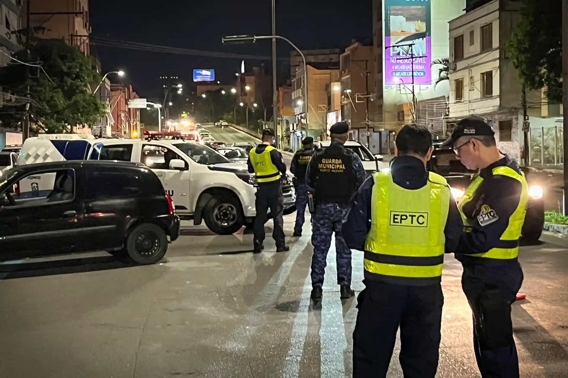 Cena noturna de Blitz Balada Segura em Porto Alegre, com agentes de segurança realizando fiscalização em veículos e garantindo a segurança no trânsito.