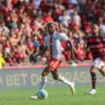 Jogadores do Internacional e Flamengo em campo durante uma partida de futebol, com torcedores ao fundo.