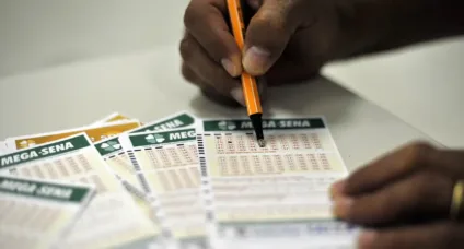 Pessoa preenchendo bilhetes da Mega-Sena, uma popular loteria brasileira, com caneta laranja.