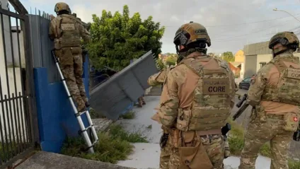 Operação policial com agentes da CORE utilizando escadas para acessar uma área restrita. A imagem retrata a ação da polícia em combate ao crime.