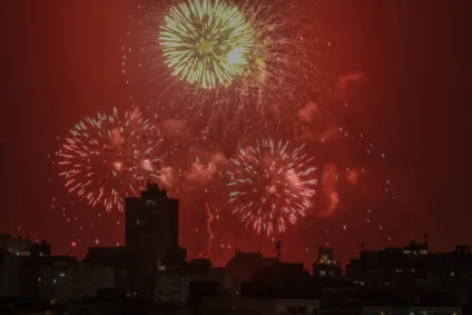 Festa com fogos de artifício iluminando o céu noturno, com explosões coloridas em meio a prédios de Porto Alegre.