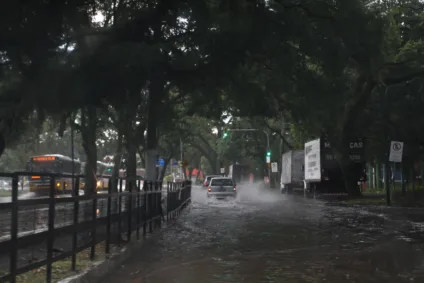 Imagem de uma rua inundada com carros e um ônibus, sob uma luz verde de semáforo, após tempestade em Porto Alegre.