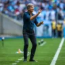 Técnico Renato Portaluppi em ação no campo, gesticulando durante uma partida de futebol, demonstrando estratégia e liderança frente à torcida.