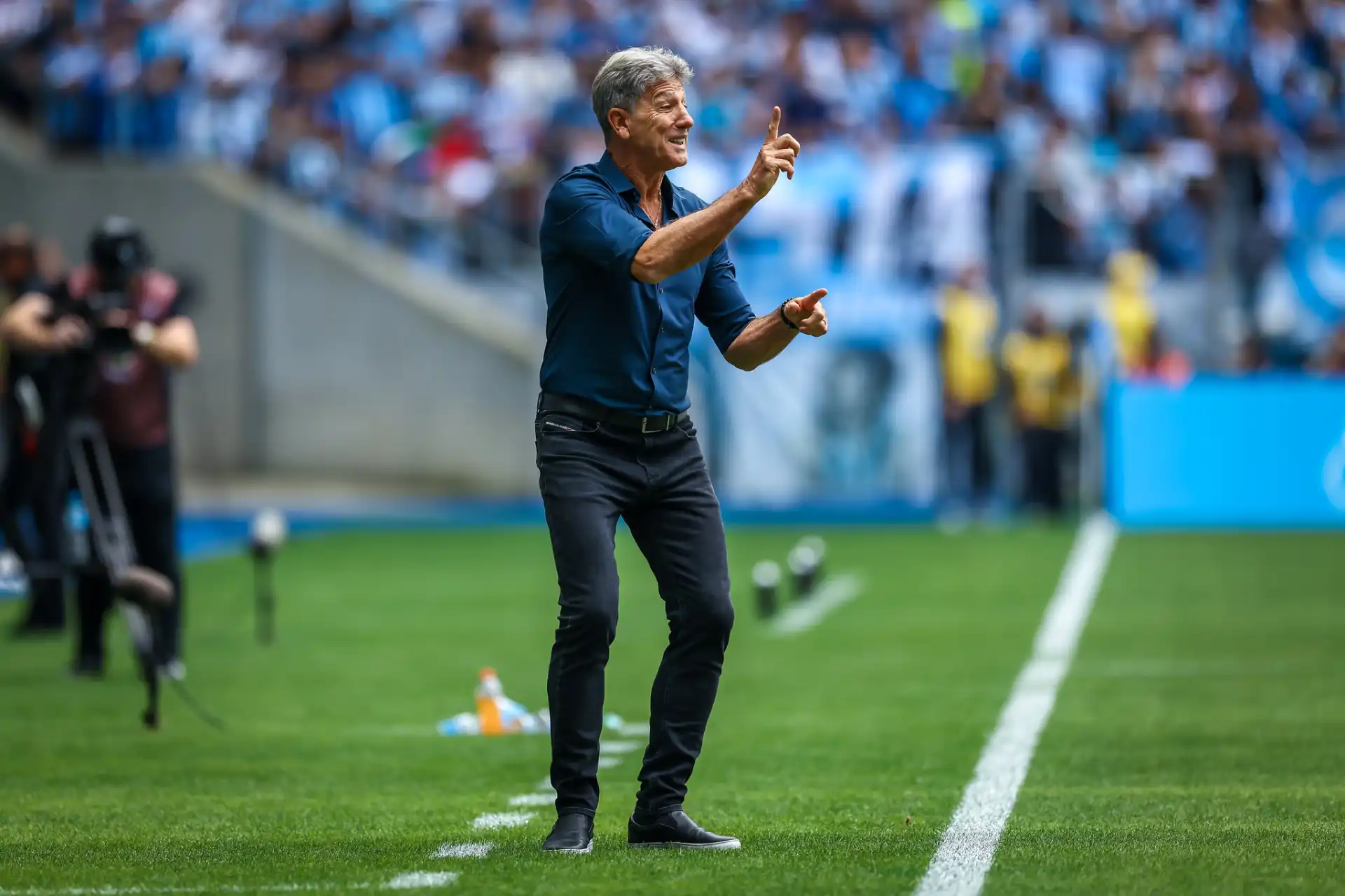 Técnico Renato Portaluppi em ação no campo, gesticulando durante uma partida de futebol, demonstrando estratégia e liderança frente à torcida.