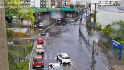 Vista da Avenida Plínio Brasil Milano, mostrando alagamento em vias urbanas com veículos tentando passar em meio à inundação após chuva intensa