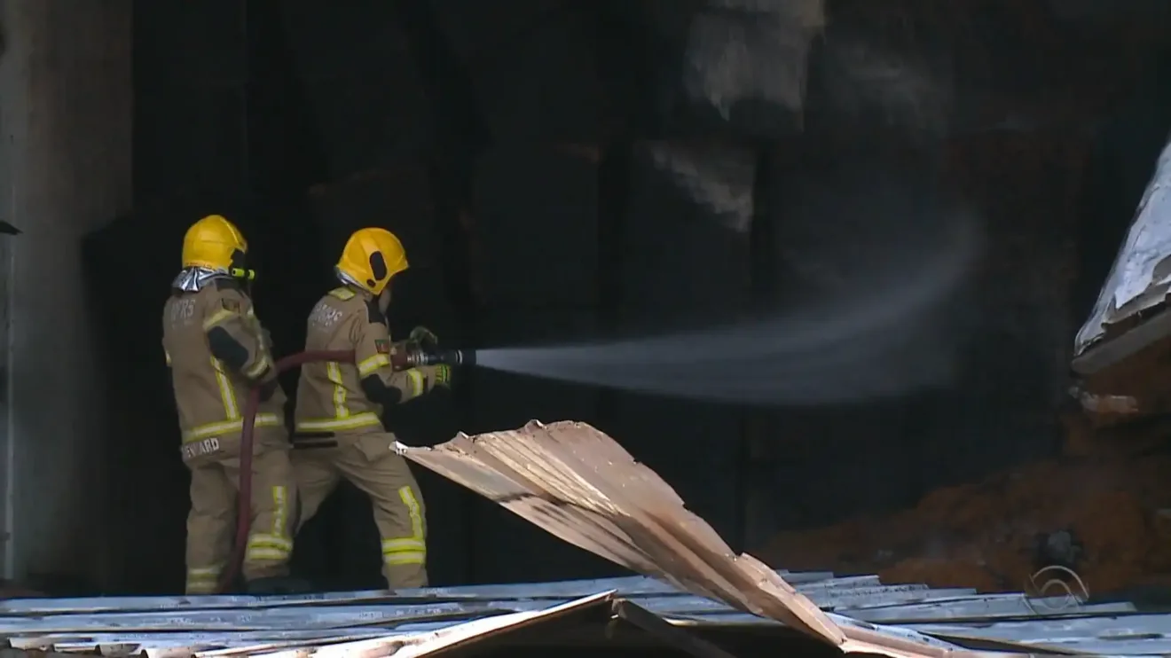 Bombeiros combatem incêndio, usando mangueira para controlar as chamas.