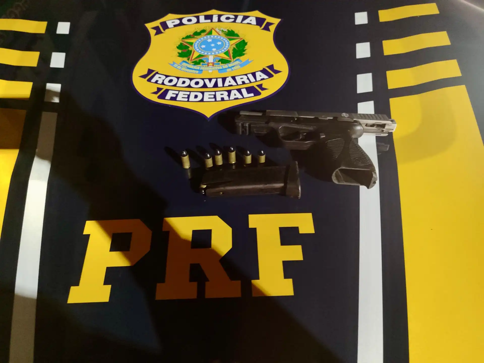 Imagem de uma arma de fogo e cartuchos sobre o capô de uma Polícia Rodoviária Federal.