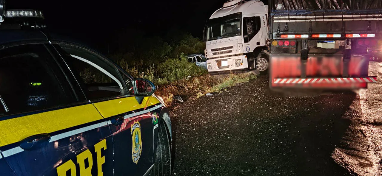 imagem de uma operação da Polícia Rodoviária Federal com um caminhão parado à beira da estrada à noite, enfatizando a fiscalização e segurança no trânsito.