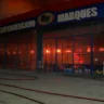 Incêndio no Supermercado Marques em Guaíba, com chamas visíveis pela fachada e equipe de bombeiros atuando na contenção do fogo.