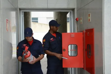 Dois bombeiros em atividade, um segurando um extintor e o outro abrindo um armário de emergência.