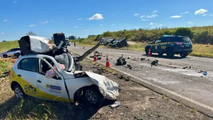 Imagem de um acidente de trânsito em uma estrada, mostrando um carro danificado, destroços e viatura da polícia rodoviária.