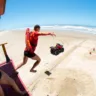 Salvamento aquático na praia, com dois salva-vidas em ação. Um salva-vidas salta da torre enquanto um quadriciclo está na areia.