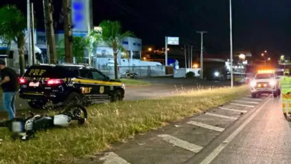 Cena noturna com viatura da PRF e uma motocicleta acidentada em rodovia.