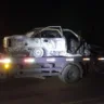 Imagem de um carro queimado sendo transportado em um caminhão durante a noite.