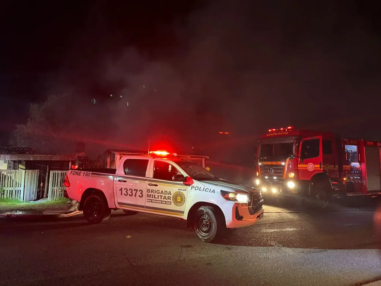 Viatura da Brigada Militar e caminhão dos bombeiros em ação durante a noite, com sirenes acionadas em situação de emergência.