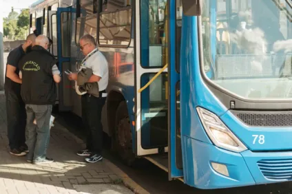 Três homens observam um ônibus azul parado, um deles verifica documentos enquanto os outros observam. O ônibus é parte do transporte público de Canoas, na região metropolitana.