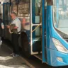 Três homens observam um ônibus azul parado, um deles verifica documentos enquanto os outros observam. O ônibus é parte do transporte público de Canoas, na região metropolitana.