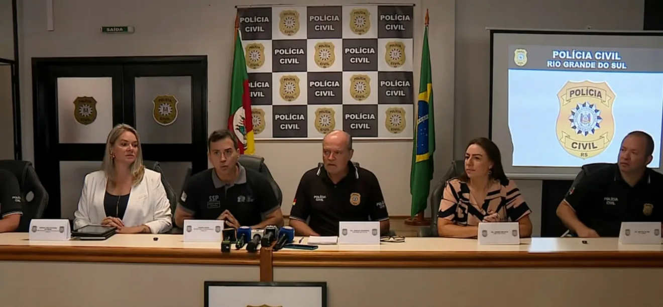 Coletiva da Polícia Civil do Rio Grande do Sul com representantes da instituição em uma sala de imprensa, acompanhados da bandeira do Brasil.