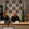 Coletiva da Polícia Civil do Rio Grande do Sul com representantes da instituição em uma sala de imprensa, acompanhados da bandeira do Brasil.