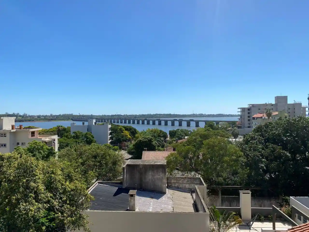 Vista panorâmica do rio Uruguai com a Ponte Internacional e prédios ao fundo em um dia ensolarado.