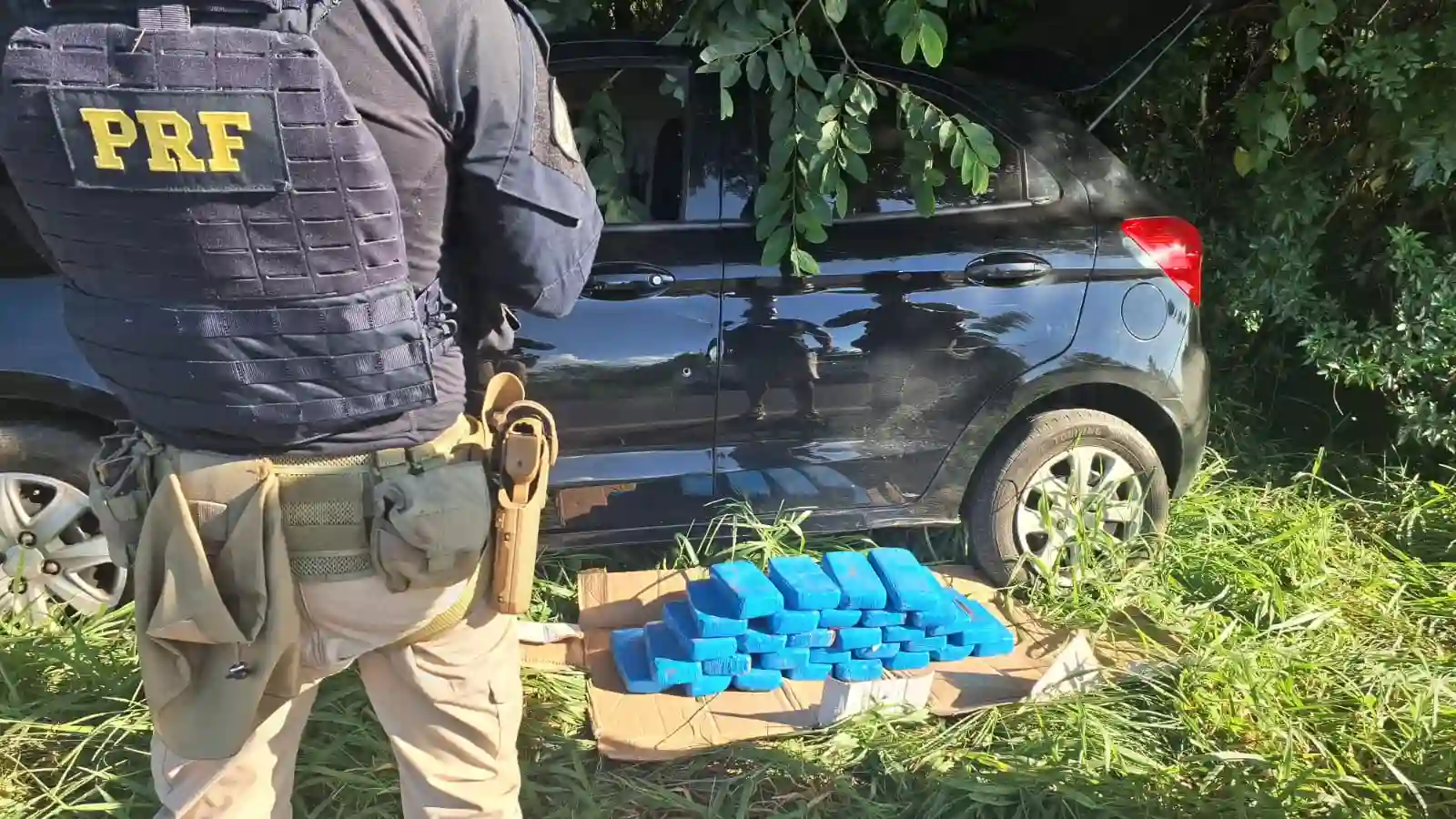 Apreensão de cocaína em Taquara, com agentes da PRF ao fundo observando os tabletes de cocaína em meio à vegetação.